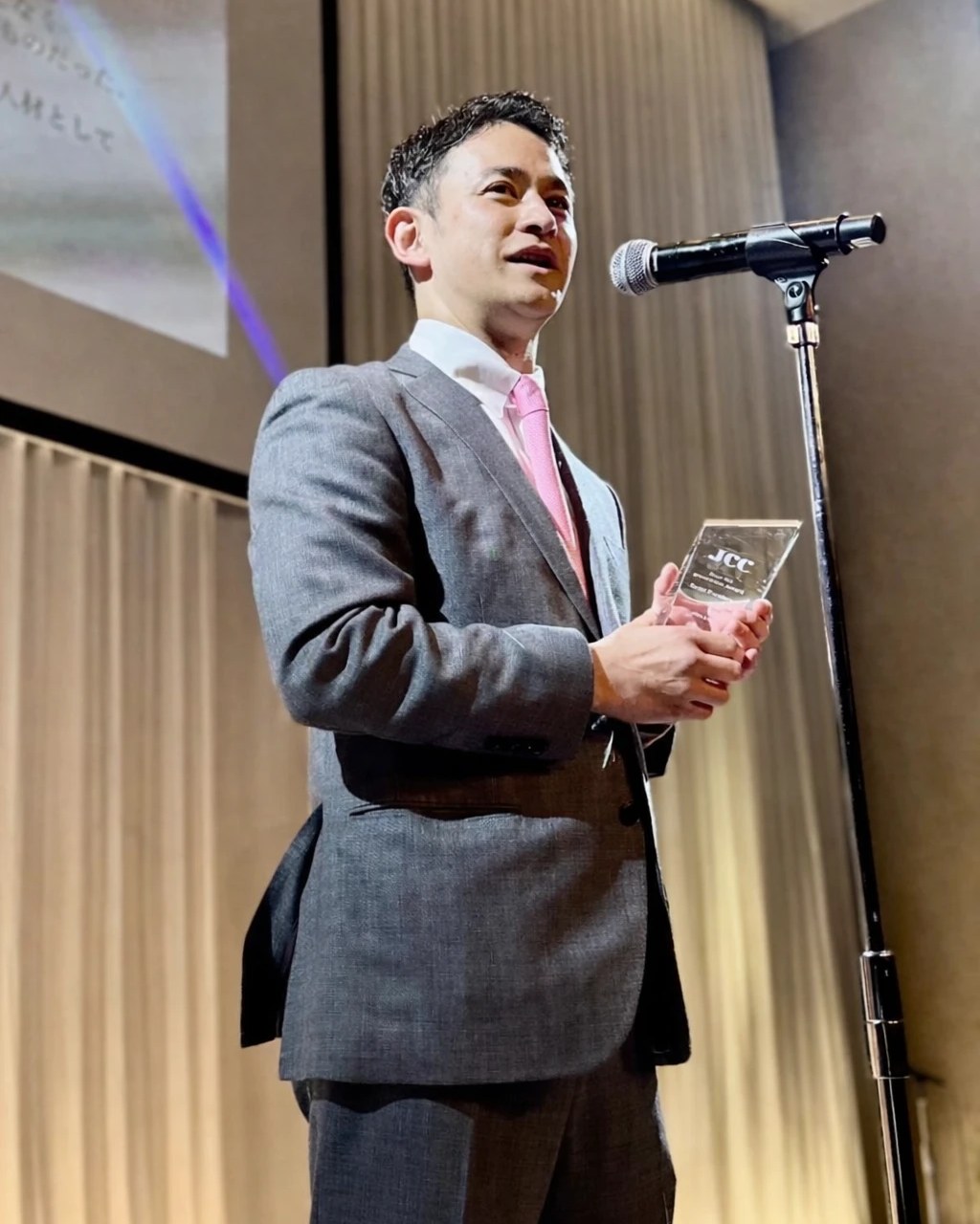 コーチ養成講座でMVPを受賞し、壇上でトロフィーを手にスピーチする代表 古川大悟